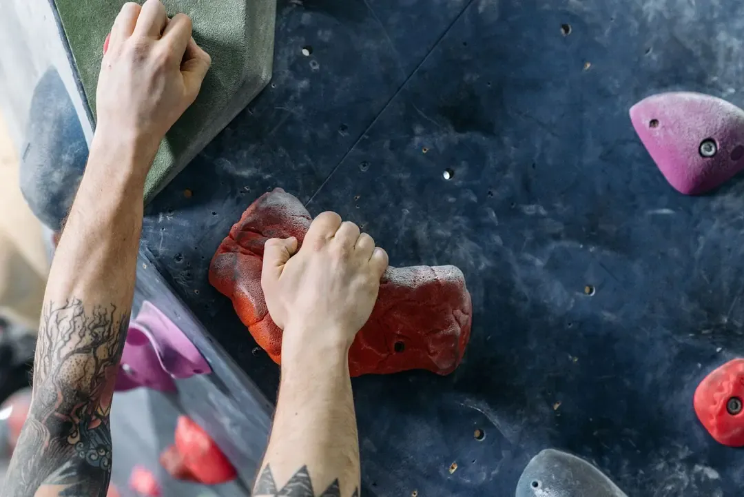 Antebrazos de un escalador con la muñeca flexionada agarrando dos presas en un muro de bloque, el gesto de agarre y pronación que carga la cara interna del codo