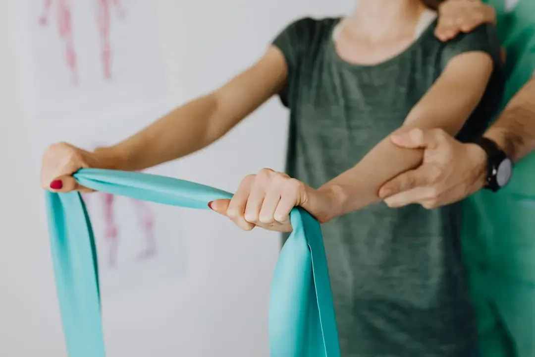 Fisioterapeuta sujetando el hombro y el codo de una paciente mientras tira de una banda elástica con los brazos extendidos